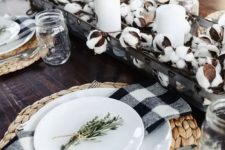 a rustic Thanksgiving table setting with woven placemats, buffalo check napkins, a cotton centerpiece with candles