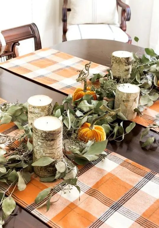 a rustic fall or Thanksgiving tablescape with bright plaid runners, greenery, orange velvet pumpkins and wooden candleholders is cool