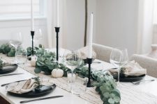 a simple Thanksgiving tablescape with a printed table runner, black plates, white napkins, greenery and white pumpkins