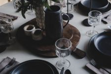 a simple and modern black and white Thanksgiving tablescape with black plates, a black jug, greenery and berries and black cutlery