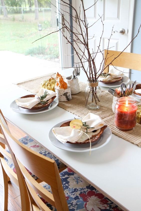 a simple woodland Thanksgiving tablescape with branches in a vase, a candle, tree branches, white plates and owl ones