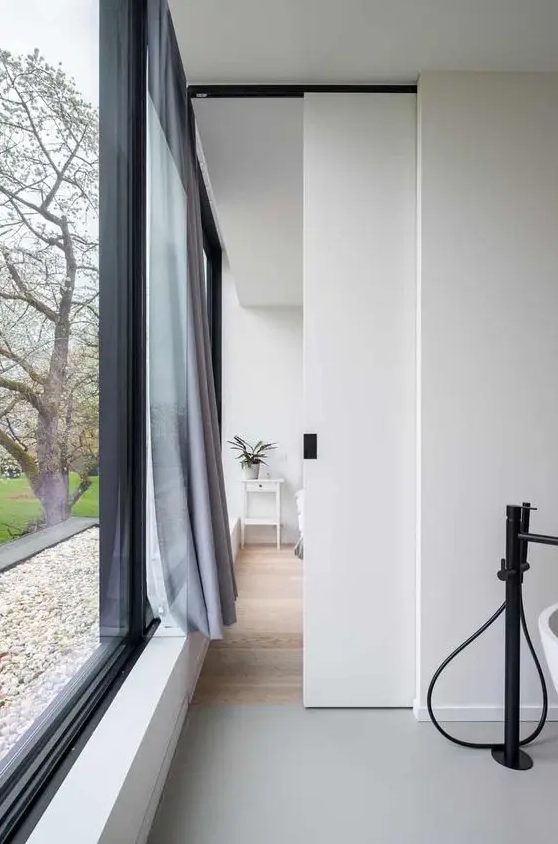 a small and delicate white pocket door with a black handle is a cool idea to hide a bathroom in a bedroom and looks cool