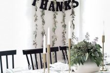 a stylish black and white Thanksgiving space with greenery, white porcelain, white candles and a black bunting
