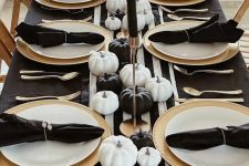 a stylish black and white Thanksgiving tablescape with a striped runner, gold chargers, gold candleholders, black and white pumpkins and black napkins