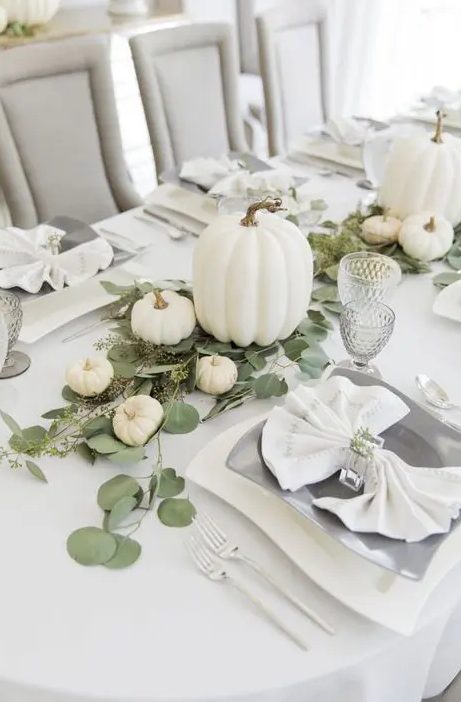 a white and neutral Thanksgiving tablescape with large and small pumpkins, eucalyptus, quirky plates and silver cutlery