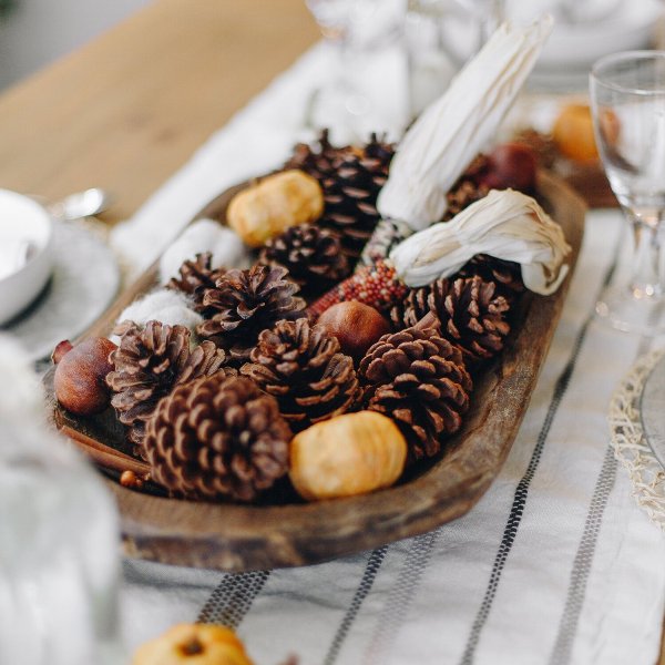 a woodland Thanksgiving centerpiece of pinecones in a bowl, pomegranates, greenery and faux pumpkins is a very cute idea