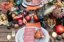 a woodland lux Thanksgiving table setting with rust napkins, fresh fruit on the table, neutral blooms and grasses plus colored glasses