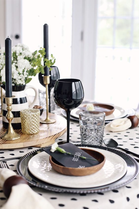 an elegant black and white Thanksgiving tablescape with a polka dot tablecloth, black and white porcelain, black glasses and candles and white blooms