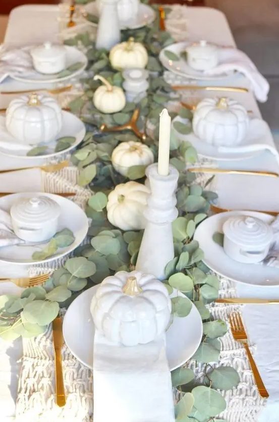 an elegant white Thanksgiving tablescape with white pumpkins, porcelain, candles, a woven table runner, a eucalyptus table runner