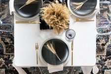 an ultra-modern black and white Thanksgiving table with black and white plates, a black runner, wheat arrangements and gold cutlery