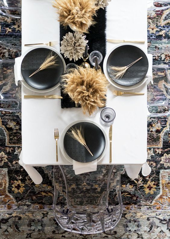 an ultra modern black and white Thanksgiving table with black and white plates, a black runner, wheat arrangements and gold cutlery