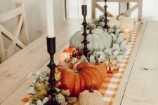 beautiful Thanksgiving table decor with a plaid runner, pale greenery, pale pumpkins and orange ones, candles is a cool idea