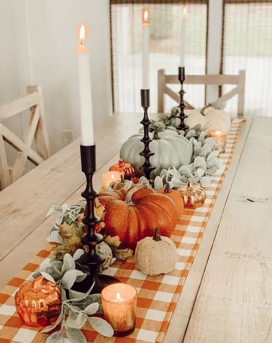 beautiful Thanksgiving table decor with a plaid runner, pale greenery, pale pumpkins and orange ones, candles is a cool idea
