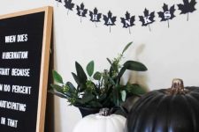 black and white Thanksgiving decor with pumpkins, a leaf-shaped bunting, a sign and greenery