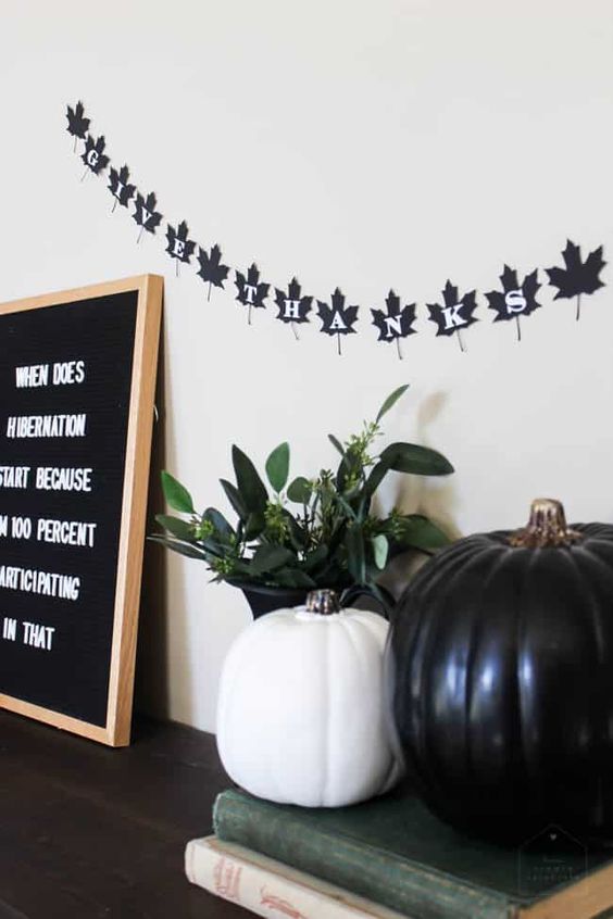 black and white Thanksgiving decor with pumpkins, a leaf shaped bunting, a sign and greenery