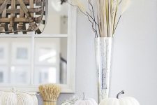 cool Thanksgiving decor with a woven tray, natural and fabric pumpkins, a silver vase with grasses and twigs