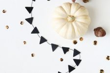 laconic fall or Thanksgiving decor with a black bunting, a white pumpkin, pinecones and gold sequins