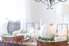 lovely white Thanksgiving tablescape with large candle lanterns, large white pumpkins, white porcelain, woven chargers and some greenery