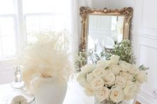 refined white Thanksgiving decor with pumpkins, blooms, dried grasses, a candle and a refined crystal chandelier