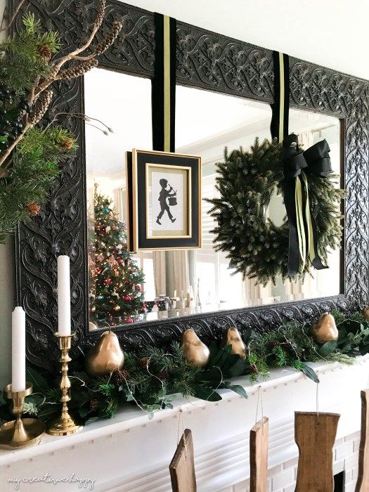 lovely black, gold and green Christmas decor with an evergreen garland with lights, gilded pears, an evergreen wreath with a black bow