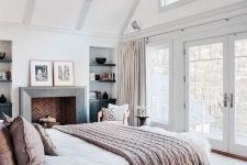 03 a beautiful and airy bedroom with a brick clad fireplace, a bed with white and dusty pink bedding, niche shelves, wooden beams