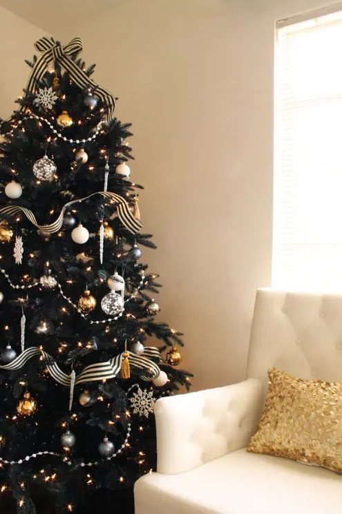 a chic and refined black Christmas tree with lights, black, gold and white ornaments and snowflakes and beads
