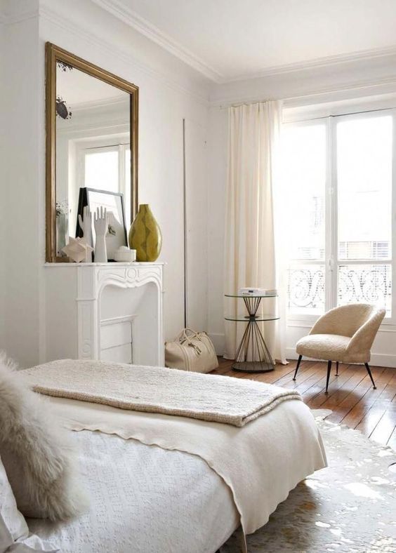 a beautiful and refined Parisian bedroom with a non-working fireplace, an oversized mirror, a bed with layered bedding and a faux fur rug