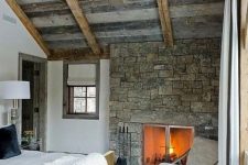 08 a welcoming chalet bedroom with a weathered wooden ceiling with beams, a stone accent wall with a fireplace and mid-century modern furniture