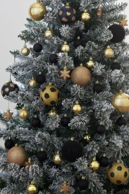 a flocked Christmas tree decorated with gold and black ornaments, babules and stars is a very chic and bold idea