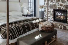 09 a modern rustic bedroom with a stone accent wall with a fireplace, a canopy bed, a leather bench, a large rug