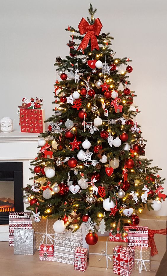 a traditional Christmas tree in Scandinavian style, with red and white ornaments of glass and felt, pinecones, lights and a large red bow