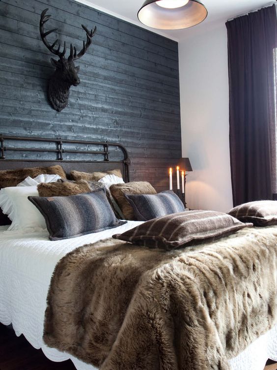 a gorgeous chalet bedroom with a black wood accent wall, a forged bed styled with layered bedding and dark curtains