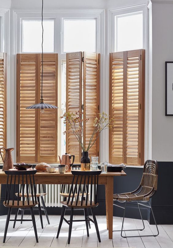 a modern neutral dining space with light-stained part shutters that echo with the dining table, with stained and black chairs