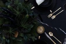 19 a moody and very elegant Christmas tablescape with an evergreen centerpiece, tall and thin candles, gold cutlery and candlholders, black plates and chargers