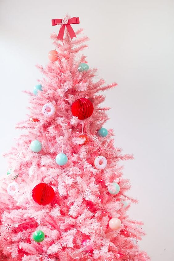 a pink Christmas tree with mini blue and green ornaments, with red paper balls and pink donut ornaments is a fun candy-inspired decor idea