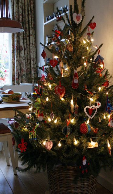 a Scandinavian Christmas tree with felt red and white ornaments, lights and a basket instead of a tree skirt is a traditional idea