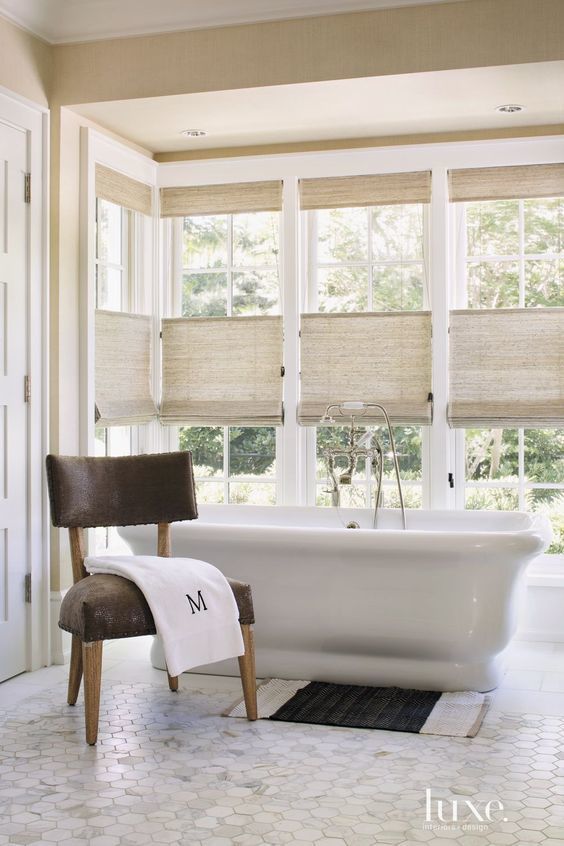 a beautiful neutral farmhouse bathroom with a whole glazed niche that is made more private with natural woven shades, which also add a textural touch