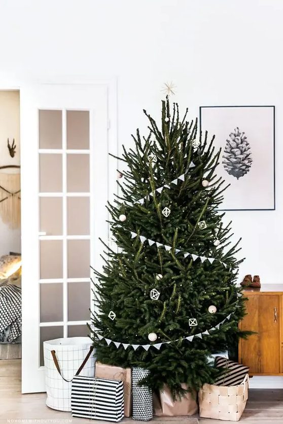 a modern Scandi tree with buntings, white and wooden ornaments and a star on top plus lights proves that less is more as it looks fantastic