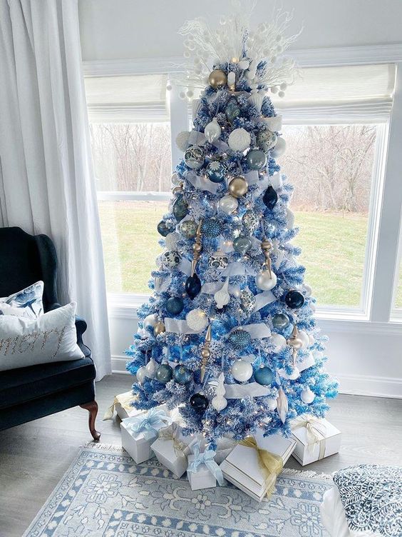an icy blue Christmas tree decorated with pale and navy ornaments, white, gold and silver ones plus frosted branches with pompoms on its top is a creative idea