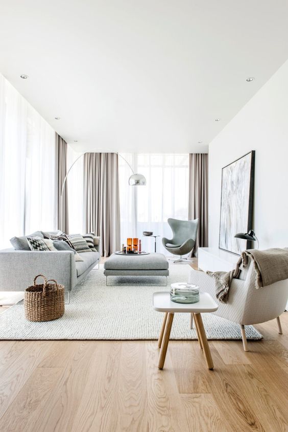 a Scandinavian living room with light grey curtains that highlight the high ceiling, light grey furniture and a large statement rug