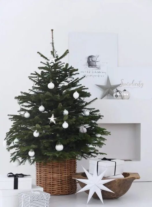 a modern Scandinavian Christmas tree with white ball and star ornaments in a basket looks very laconic and chic