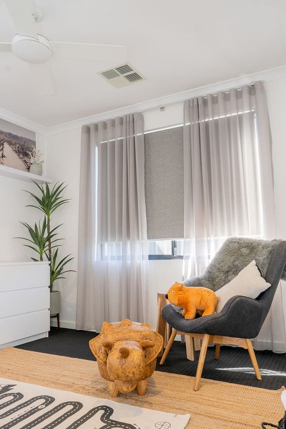 a kid's space with a window treated with grey blinds and semi sheer light grey curtains that are mainly for decor
