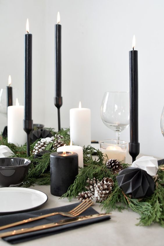 a Scandinavian Christmas table setting with black napkins, candles and bowls, black and white faceted ornaments and elegant cutlery