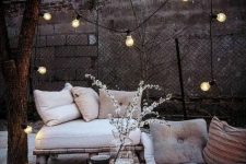 a Scandinavian winter terrace with a loveseat, lots of cushions and pillows, candle lanterns, a bulb garland and some blooms