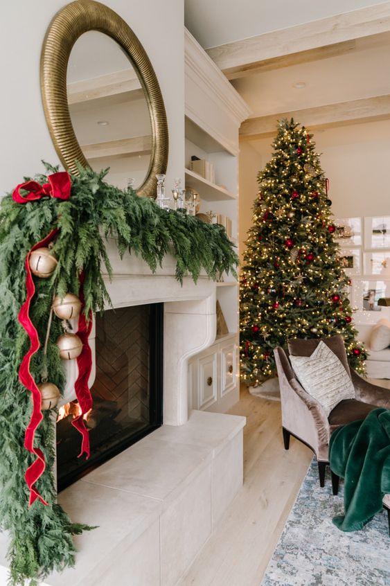 a beautifully dressed Christmas mantel with a lush evergreen garland, red velvet ribbons and oversized bells is a traditional and chic idea