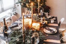 a black and gold party table with dark linens, white porcelain, gold cutlery, candleholders and evergreens