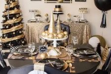 a black and gold tablescape with shiny and glitter ornaments and cone trees, black plates and chargers