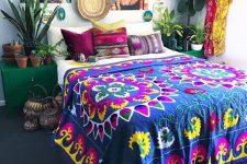 a boho maximalist bedroom with a navy carpet on the floor, emerald nightstands, a bold gallery wall, potted plants and bright textiles