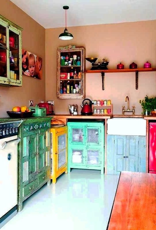 a boho maximalist kitchen with dusty pink walls, colorful mismatching cabinets and colorful cookware is amazing