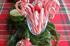 a bold and pretty festive centerpiece of greenery, fir branches, red ornaments, candles and candy canes is very chic